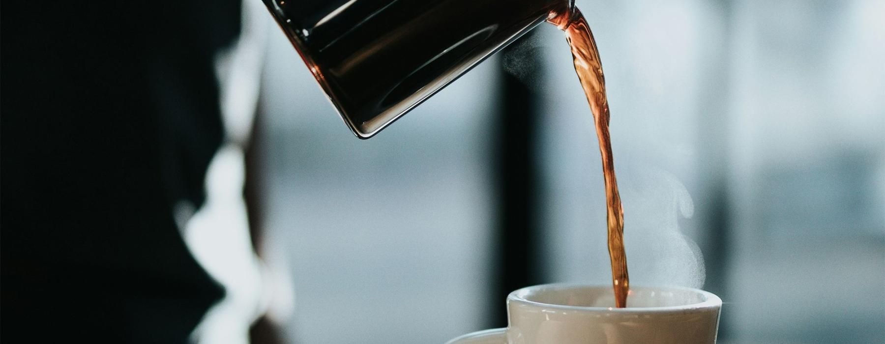 a person pouring a carafe of coffee into a cup